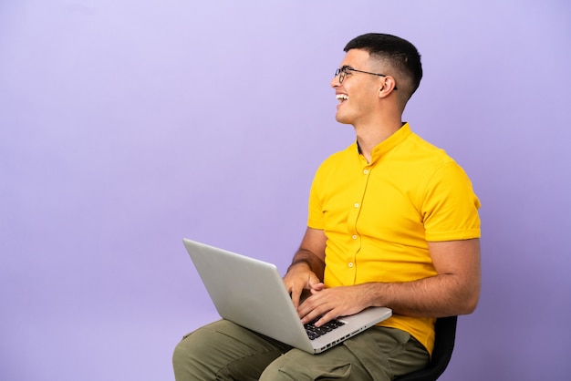 Young man sitting on a chair with laptop laughing in lateral position