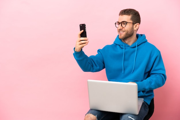 젊은 남자는 selfie를 만드는 노트북으로 의자에 앉아