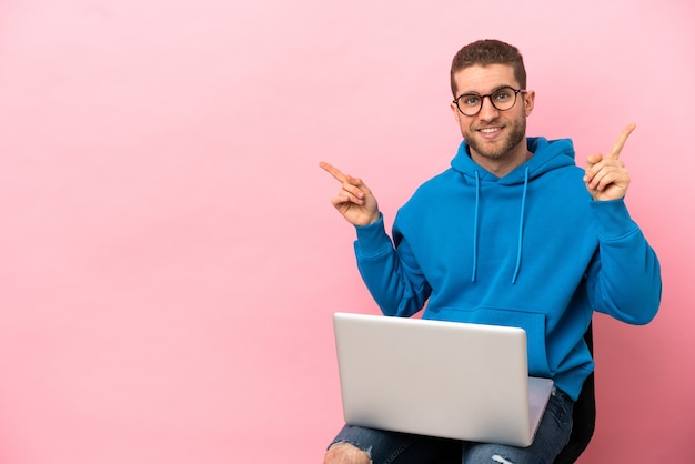 Young man sitting on a chair with laptop pointing finger to the laterals and happy