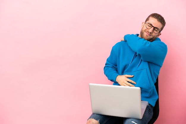 Young man sitting on a chair with laptop suffering from pain in shoulder for having made an effort