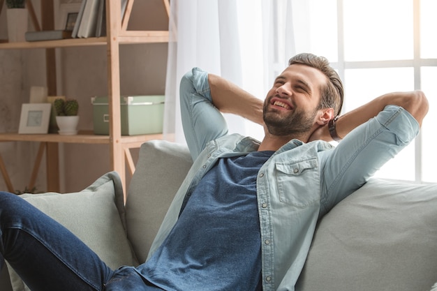 コーチに座っている若い男は家で休む