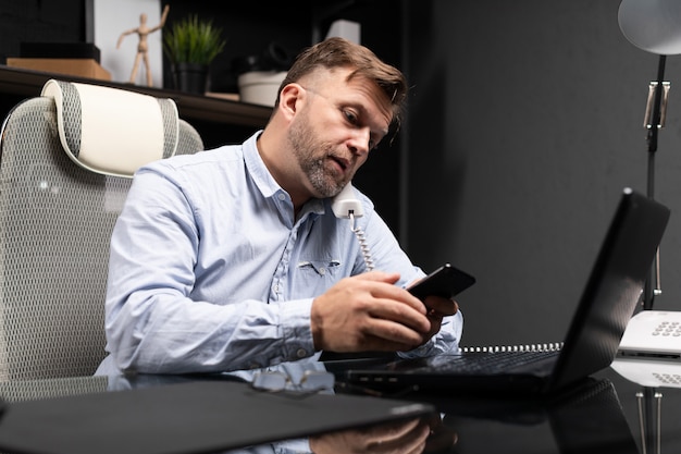 Young man sitting at computer Desk and holding landline phone and mobile phone