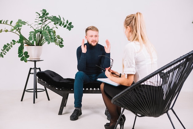 Photo young man sitting on couch discussing with female psychotherapist his problems