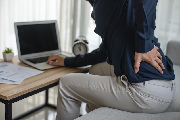 Young man sitting at the desk He used hand holding to press down on the lower back