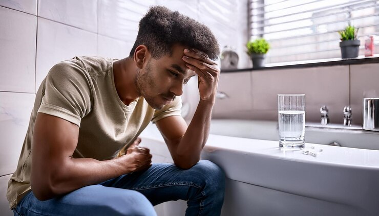 Photo a young man sitting on the edge of a bathroom bathtub looking pale and exhausted