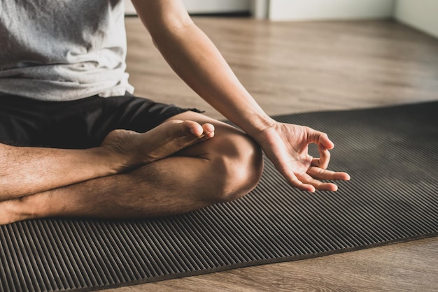 Young man sitting on the exercise mat practicing meditation in a lotus pose alone at the gym in the morning He was closing his eyes slowly breathing in and out