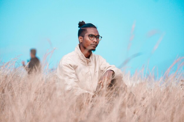 Young man sitting on field under the sky