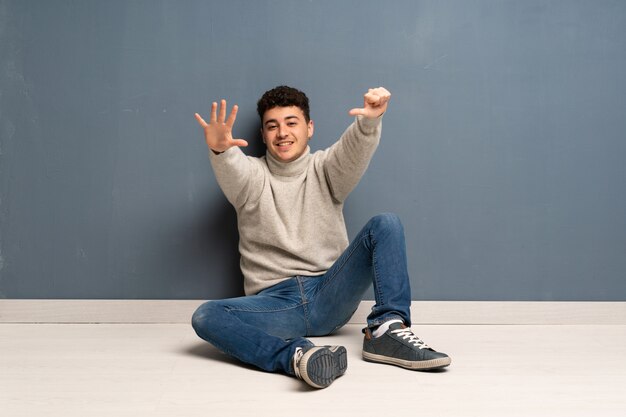 Young man sitting on the floor counting six with fingers