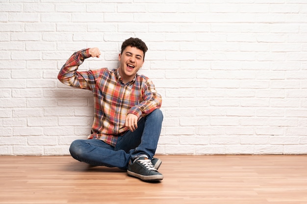 Young man sitting on the floor doing strong gesture