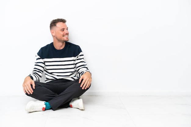 Photo young man sitting on the floor isolated on white background in lateral position