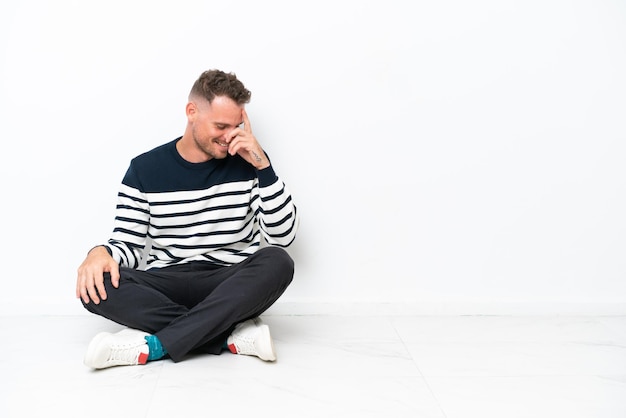 Young man sitting on the floor isolated on white background laughing