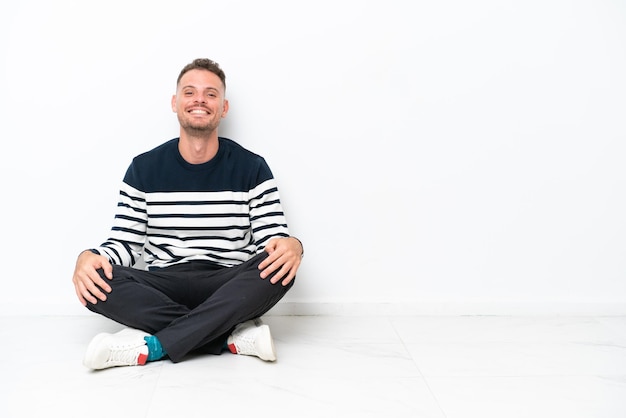 Young man sitting on the floor isolated on white background laughing