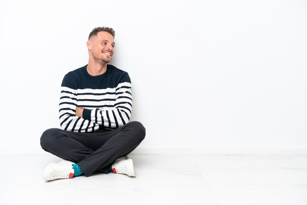 Photo young man sitting on the floor isolated on white background looking side