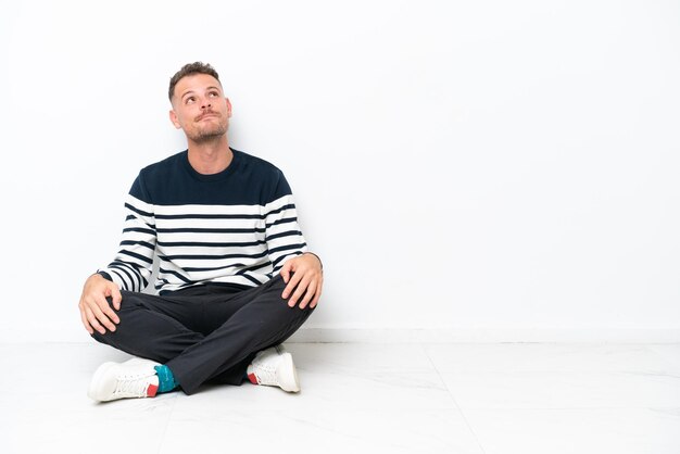 Photo young man sitting on the floor isolated on white background and looking up