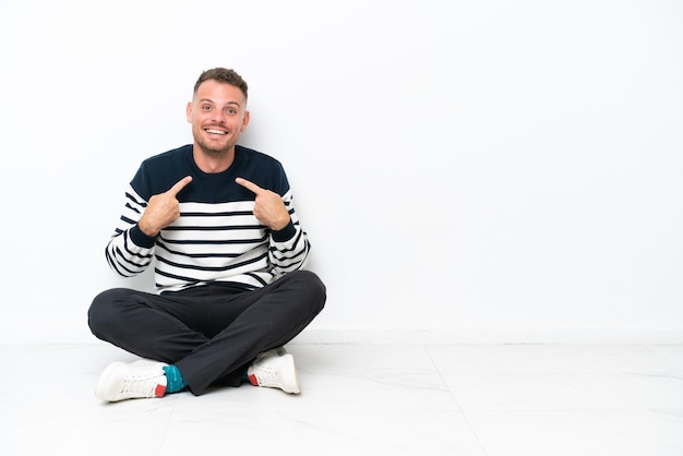 Young man sitting on the floor isolated on white background with surprise facial expression