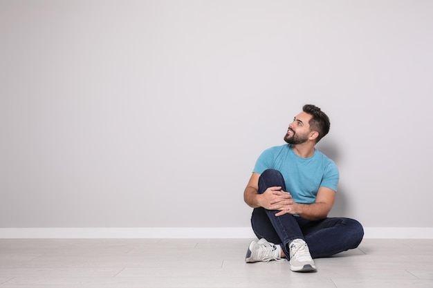 Young man sitting on floor near light grey wall indoors Space for text