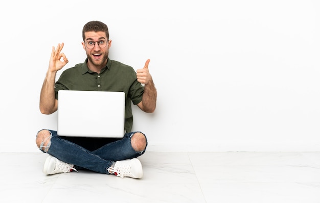 Young man sitting on the floor showing ok sign and thumb up gesture