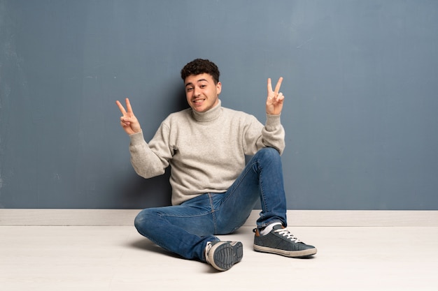 Young man sitting on the floor showing victory sign with both hands