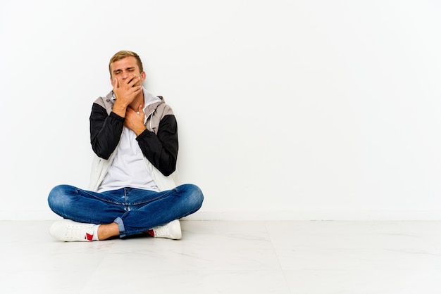 Young man sitting on the floor suffers pain in throat due a virus or infection