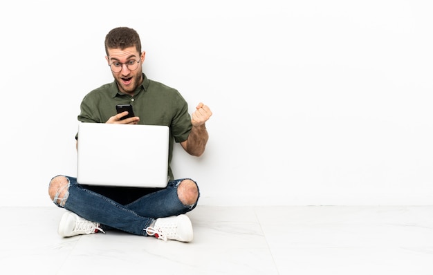 Young man sitting on the floor surprised and sending a message