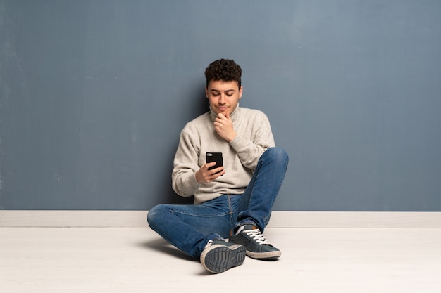 Young man sitting on the floor thinking and sending a message