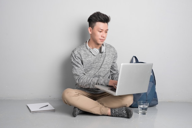 Photo young man sitting on the floor and using laptop.