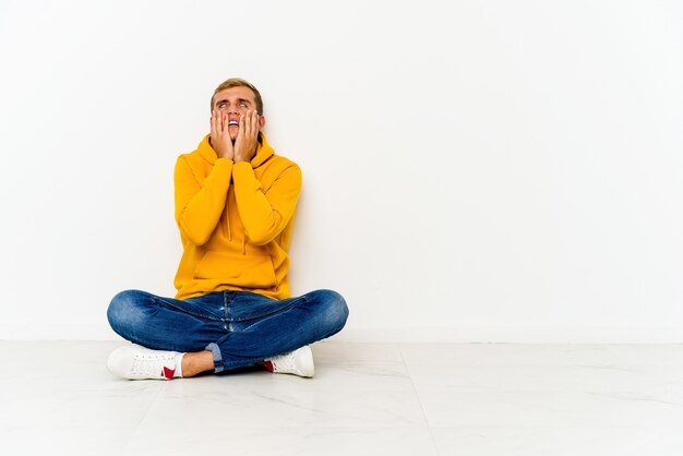 Young man sitting on the floor whining and crying disconsolately