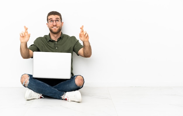 Young man sitting on the floor with fingers crossing and wishing the best