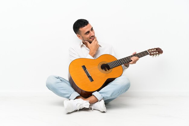 Young man sitting on the floor with guitar looking side