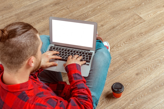 Giovane che si siede sul pavimento con il computer portatile