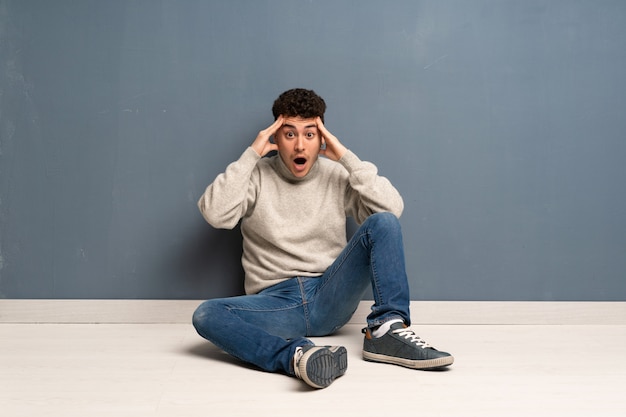 Young man sitting on the floor with surprise expression