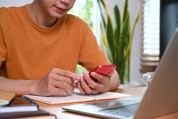 Young man sitting in front of laptop computer and using smart\
phone in living room