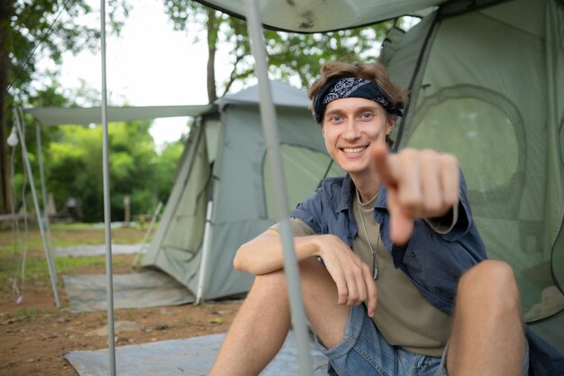 Giovane seduto di fronte alla tenda in un campeggio in campagna