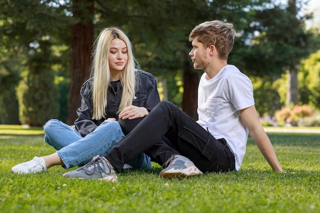 若い男が彼のガール フレンドと一緒に芝生の上に座って、彼女を見て