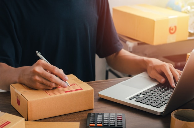 Young man sitting at home packing to be sent by post Ready to write the customer contact address from the notebook to send the destination.