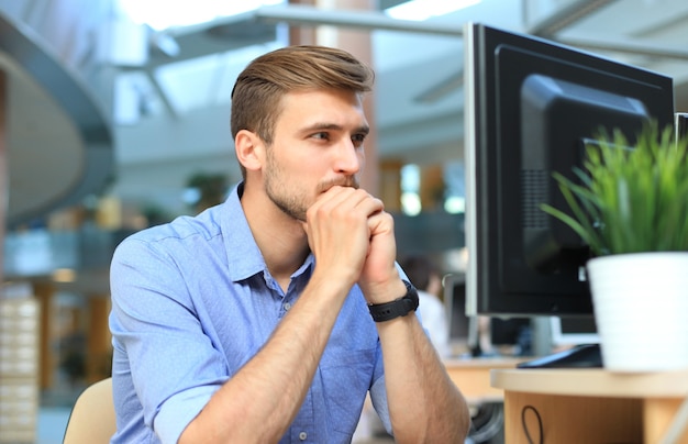 Young man sitting and looking at computer monitor while working in office.