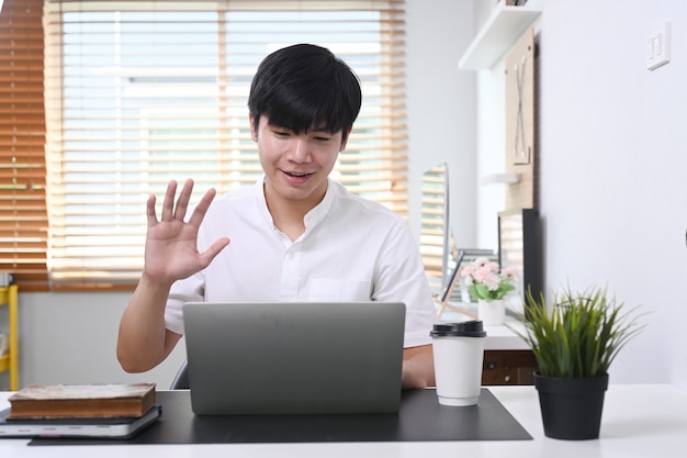 Young man sitting in modern office and video conference with his colleagues on laptop computer.