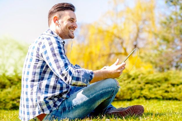 Young man sitting outdoors listening to music.He is sitting in the park.