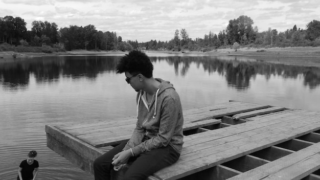 Young man sitting on pier over lake