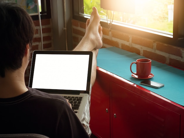 Young man sitting and play with laptop and cup of coffee in rest room. blank display screen.