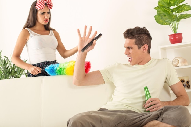 Young man sitting on sofa and watching tv. His angry wife yelling.