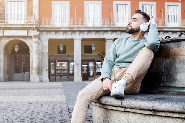 Foto giovane seduto per strada ad ascoltare musica con cuffie wireless