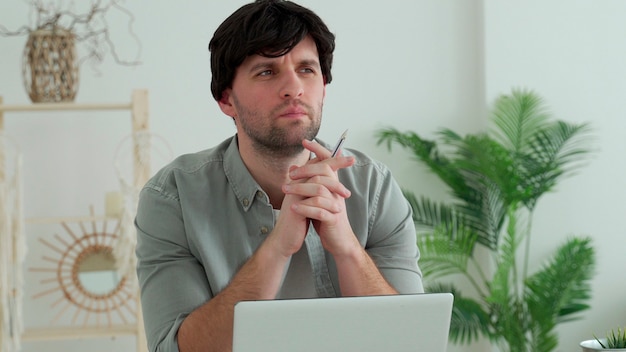 Young man sitting at the table in front of computer and thinking of inspiration search problem solution ideas