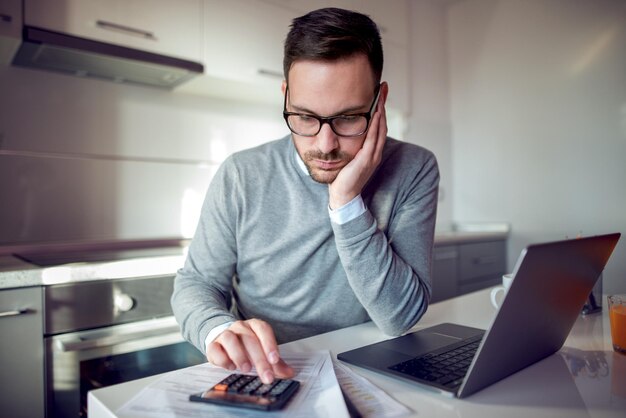 Young man sitting at table in the kitchen with laptop