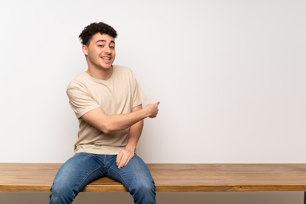 Young man sitting on table pointing back