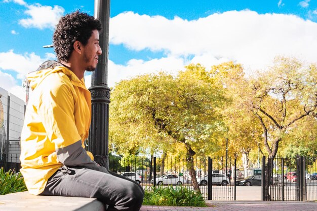 Young man sitting thinking and smiling dressed in yellow with the sky in the background in a plaza