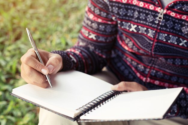 Young man sitting and using pen to write on notebook