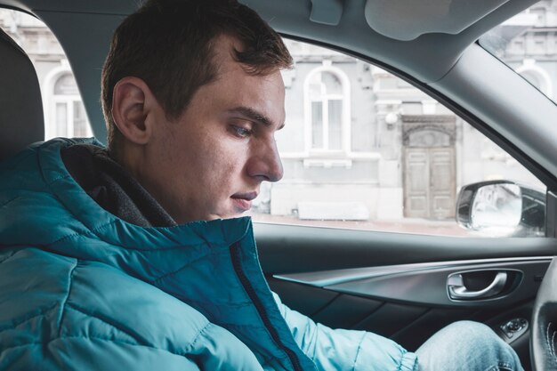 Giovane uomo seduto al volante di un'auto in una giacca