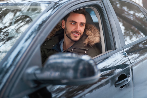 彼の車のホイールに座っている若い男