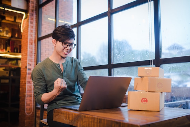 Young man sitting with computer and mobile phone on wooden floor with parcel selling ideas concept online.